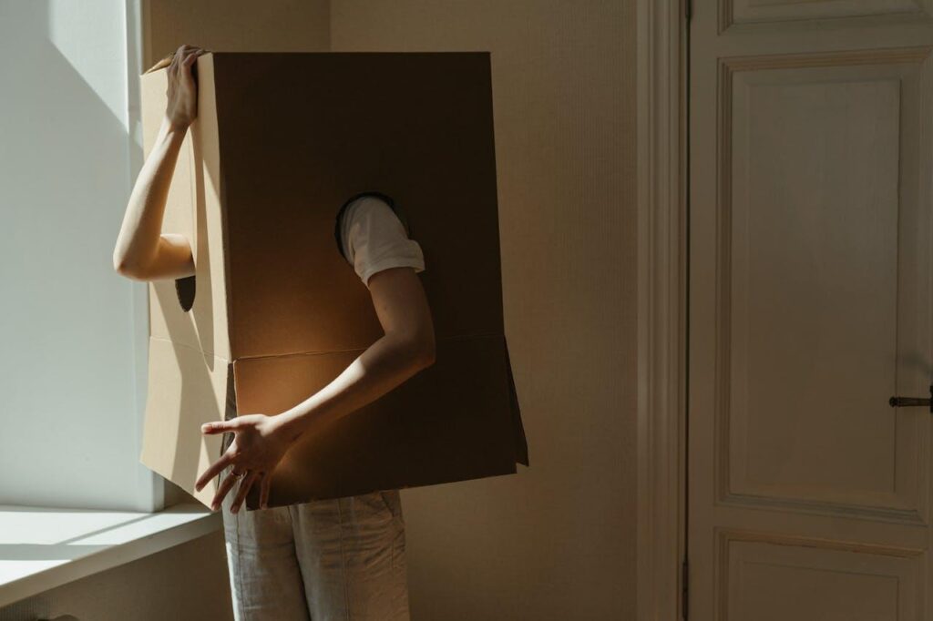 Person, die in einer Kiste versteckt ist. Nur ihre Arme und Beine schauen heraus.